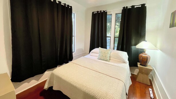 Une chambre à coucher avec un lit, des rideaux noirs, une fenêtre et une lampe de chevet.