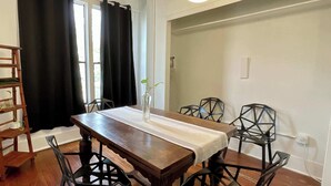 Un coin repas avec une table en bois, des chaises noires, un vase avec une plante et un luminaire suspendu.