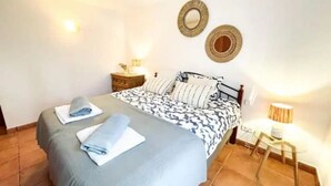 A neatly made bed with a patterned bedspread and pillows, a bedside table with a lamp, and two wall-mounted mirrors.