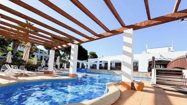 A pool area with a pergola, lounge chairs, and a clear blue pool.