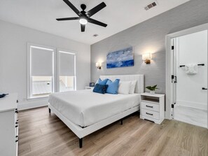 Une chambre à coucher avec un lit blanc, un ventilateur de plafond, une table de chevet et un luminaire fixé au mur.