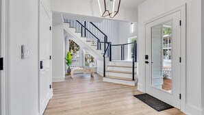 A spacious hallway with a wooden floor, a staircase with black railings, and a modern light fixture. - Private Pool, Carriage House, and Near the Beach (Destin)