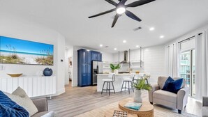 A modern living room with a large ceiling fan, a dining area with bar stools, and a kitchen with white cabinets. - Private Pool, Carriage House, and Near the Beach (Destin)