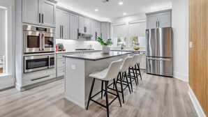 A modern kitchen with grey cabinets, stainless steel appliances, a central island with bar stools, and a wooden accent wall. - Private Pool, Carriage House, and Near the Beach (Destin)