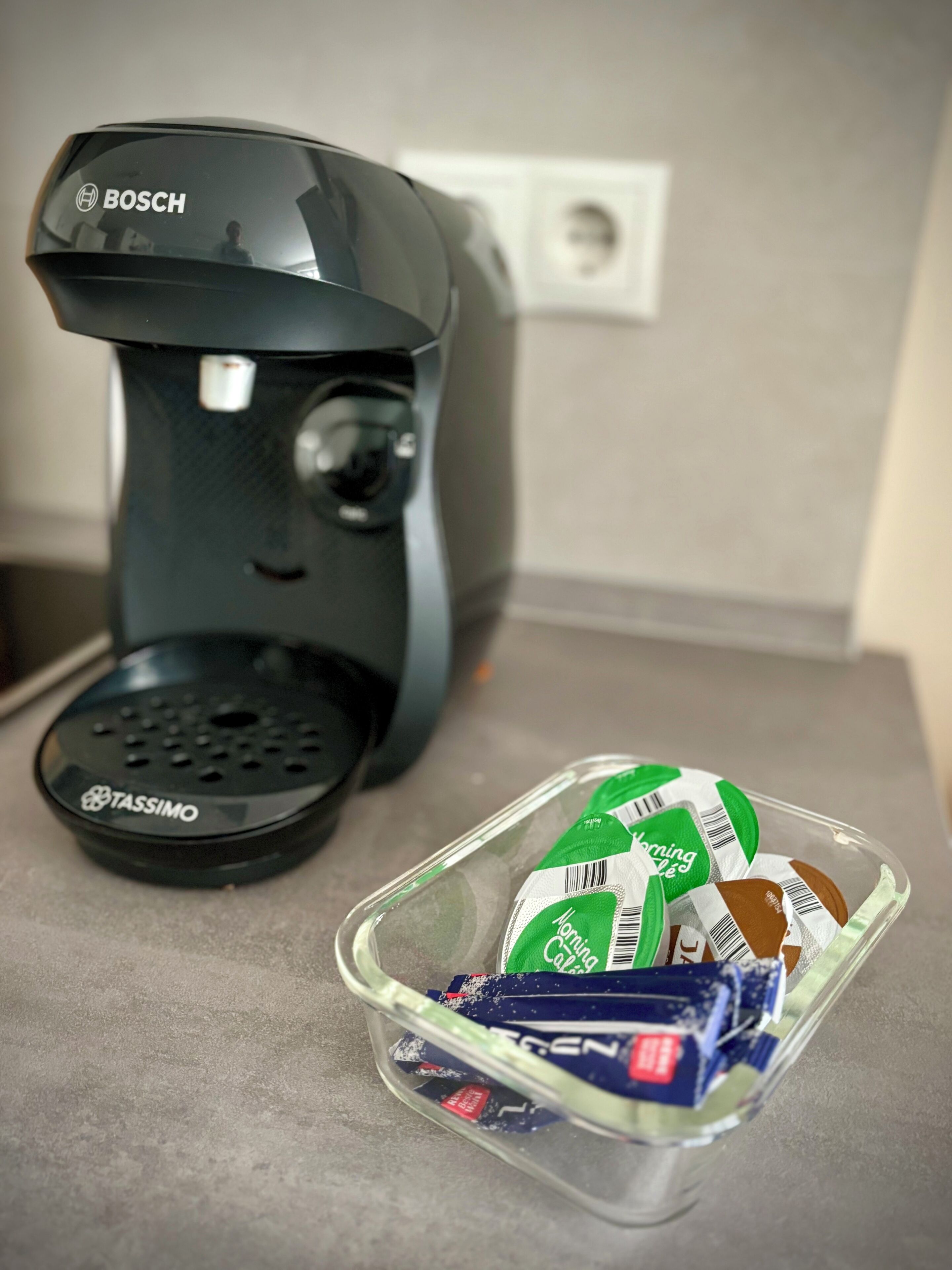 Een koffiezetapparaat en een bak met koffiekapsules op een aanrecht.