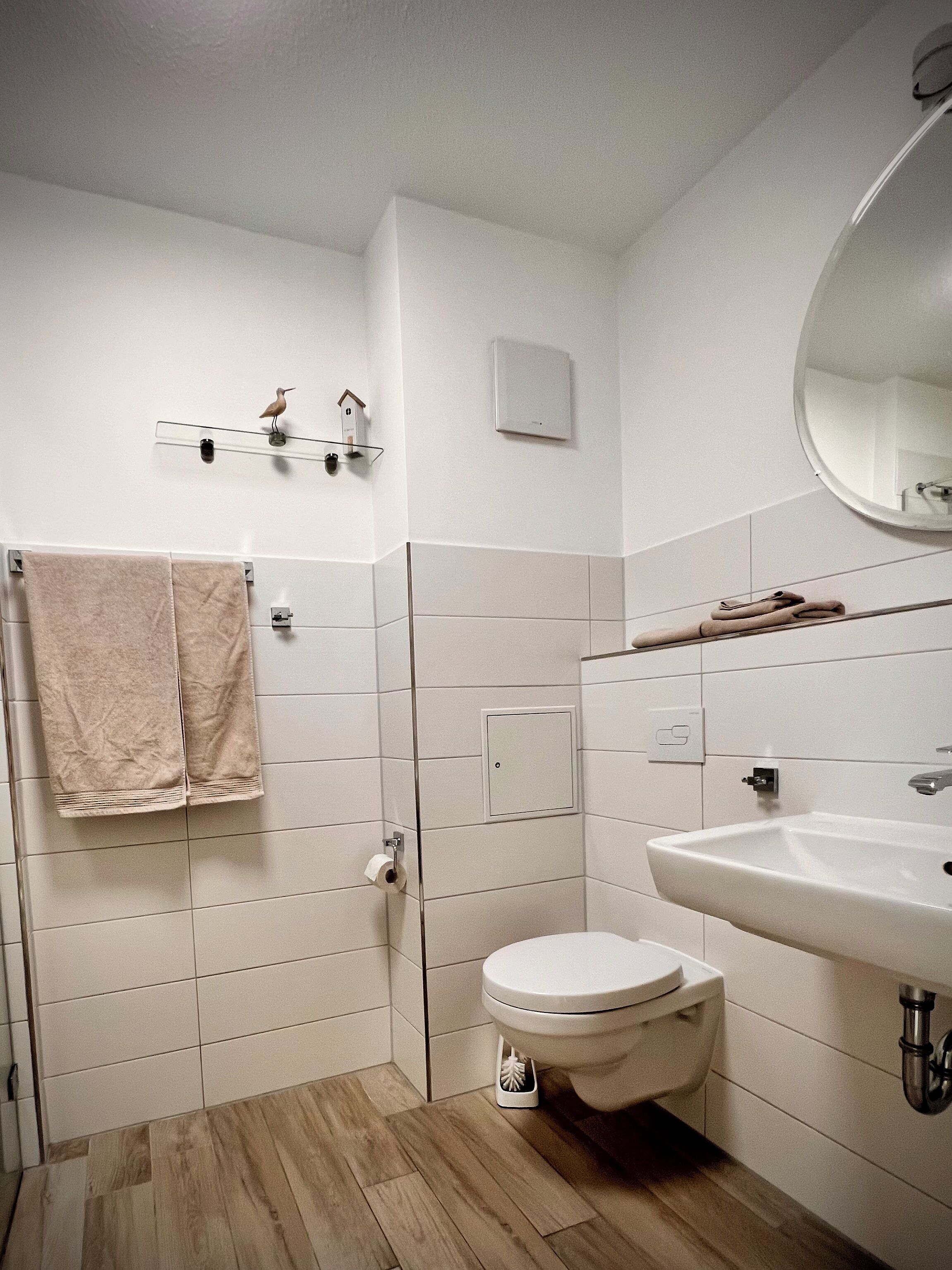 Ein Badezimmer mit Toilette, Waschbecken und Spiegel. Handtücher hängen an einem Wäscheständer und an der Wand ist ein Vogelhaus angebracht.