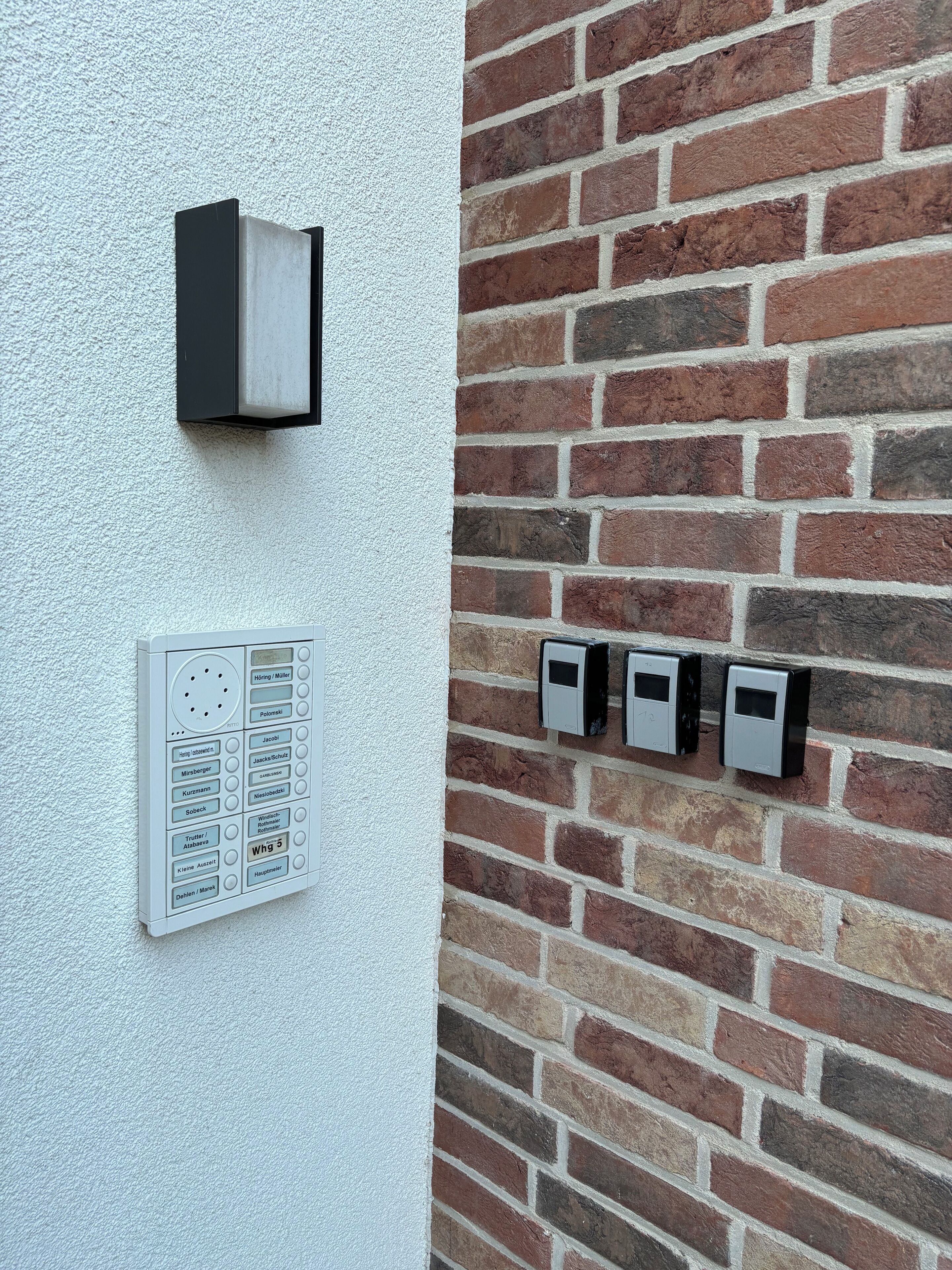 Et vægmonteret intercomsystem og et panel med flere knapper, sandsynligvis til adgang eller kommunikation.
