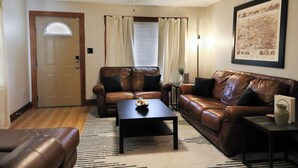 Un salon avec un canapé en cuir marron, une table basse noire et un ventilateur de plafond.