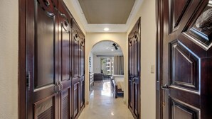 A hallway with dark wooden doors, a tiled floor, and a view into a room with a bed and a sofa.