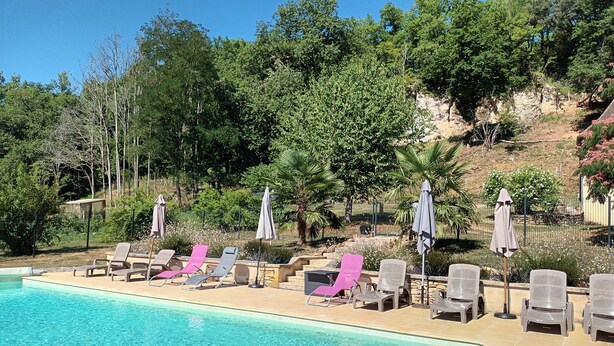 A pool area with lounge chairs and umbrellas, surrounded by trees and a hillside.