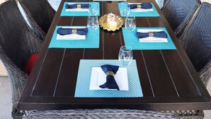 Une table à manger dressée avec des sets de table, des serviettes et de la verrerie, entourée de chaises en osier.