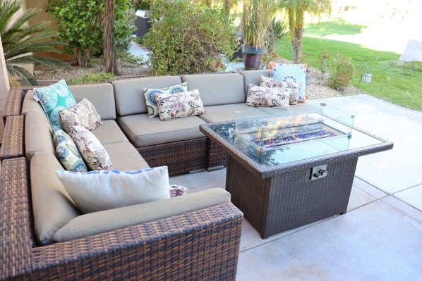 An outdoor seating area with a glass-top coffee table and a wicker sofa with multiple cushions.