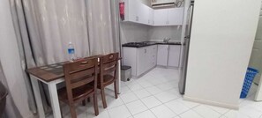 A small kitchen with a dining table and chairs, a water bottle, and a trash bin.
