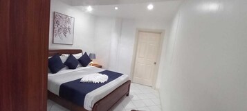 Quarto com cama, mesa de cabeceira, luminária na parede e porta.