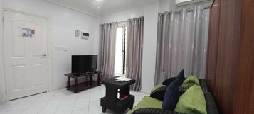 Uma sala de estar com televisão, uma mesinha, um sofá e uma porta.
