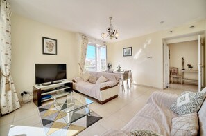 A living room with a TV, sofa, and dining area. - Lumineux 3 pièces proche centre ville A2B237 (Cannes)