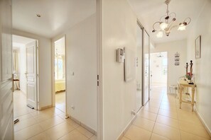 A spacious hallway with a chandelier, a dining area with a table and chairs, and a view into another room. - Lumineux 3 pièces proche centre ville A2B237 (Cannes)