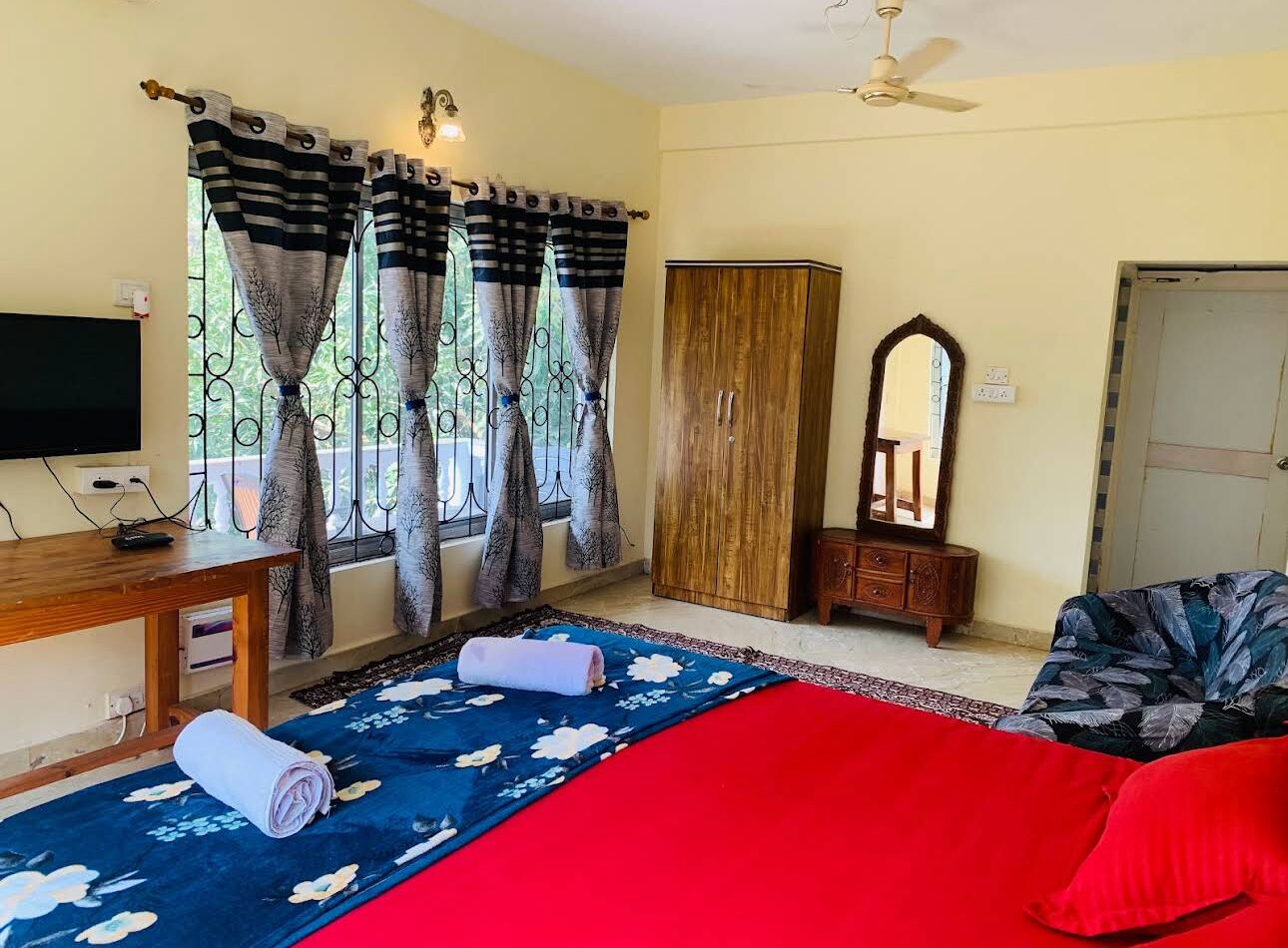Una habitación con cama, televisión, armario, espejo y ventana con cortinas.