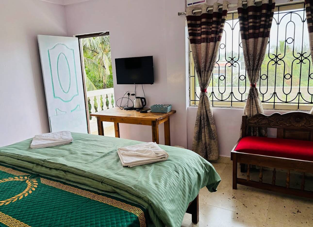 Un dormitorio con una cama, un banco de madera, una mesa con televisor y una ventana con cortinas.