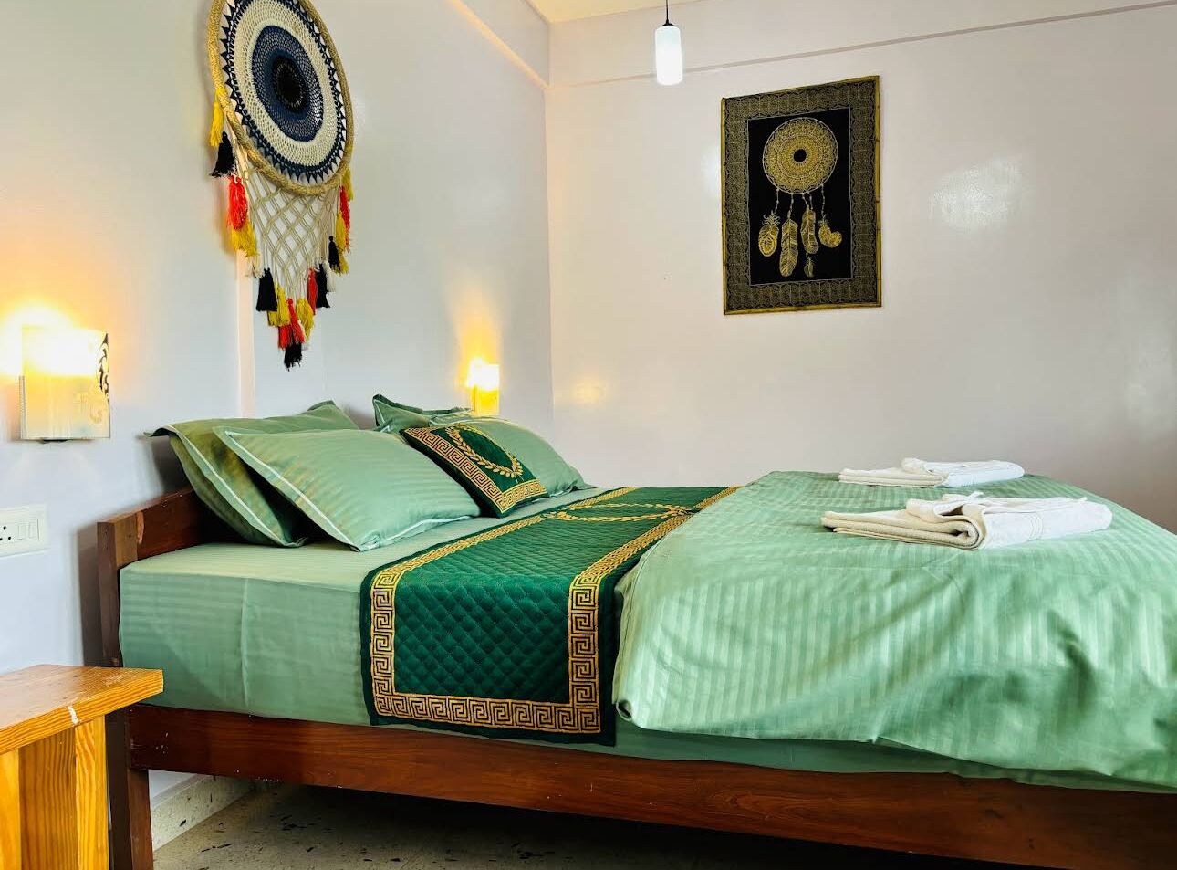 A room with a bed, two wall-mounted lights, and a dreamcatcher on the wall.