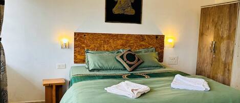 Un letto rifatto con cura, copriletto verde e due asciugamani bianchi, una testiera in legno e un'opera d'arte appesa al muro.