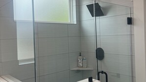Et moderne badeværelse med en glasbrusekabine, et hvidt toiletbord og en håndklæderække.