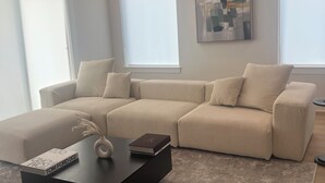 En moderne stue med en beige hjørnesofa, et sort sofabord og et nutidigt abstrakt maleri på væggen.