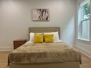 Una camera da letto con un letto, un comodino, una finestra e un quadro astratto appeso al muro.