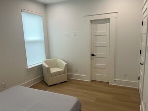 A bedroom with a bed, a chair, a door, and a window.