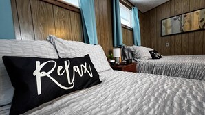 Een hotelkamer met twee bedden, houten paneelwanden, een raam met gordijnen, een nachtkastje met een lamp en een aan de muur hangend kunstwerk.