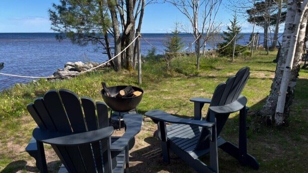 Twee Adirondack-stoelen, een klein tafeltje en een vuurkorf met houtblokken.