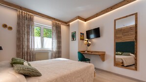 Un dormitorio con cama, escritorio, silla, televisor y un espejo grande.