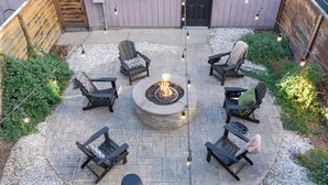 A circular outdoor seating area with a fire pit, surrounded by four Adirondack chairs and a round table.