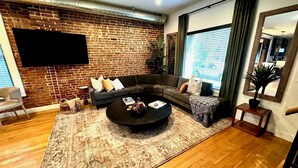 A modern living room with a brick wall, a sectional sofa, a coffee table, and a large window with curtains.