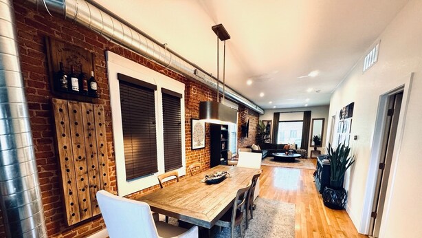 A modern kitchen with a brick wall, wooden cabinets, and a dining area with a table and chairs.