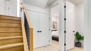 Un interior moderno con una escalera de madera, puertas blancas, una cama y una planta en maceta.