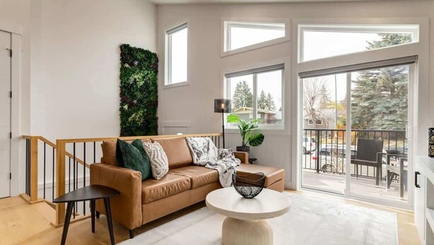 Una sala de estar moderna con un sofá beige, una mesa de centro redonda y vistas al exterior a través de amplios ventanales.