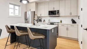 Una cocina moderna con una isla central, taburetes de bar, electrodomésticos de acero inoxidable y un microondas.
