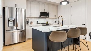 Una cocina moderna con electrodomésticos de acero inoxidable, una isla central con taburetes de bar e iluminación colgante.