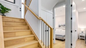 Un escalier avec des marches en bois et des rampes noires menant à une chambre à coucher où se trouvent un lit et une table de chevet.
