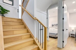A staircase with wooden steps and black railings leading to a bedroom with a bed and a nightstand. - Long Stays, Fenced Yard, Free Parking & King Bed (Calgary)