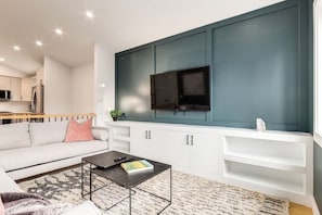 Una sala moderna con sofá, una mesa de centro y un televisor de pantalla plana montado sobre una pared de acento color turquesa.