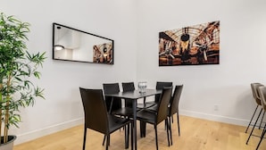Un coin repas avec une table et des chaises, une plante en pot et deux œuvres d’art encadrées accrochées au mur.