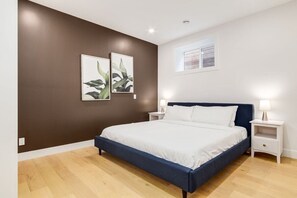 A bedroom with a large bed, two bedside tables, and wall-mounted artwork. - Long Stays, Fenced Yard, Free Parking & King Bed (Calgary)