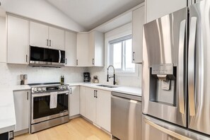 A modern kitchen with stainless steel appliances, a microwave, oven, and refrigerator. - Long Stays, Fenced Yard, Free Parking & King Bed (Calgary)