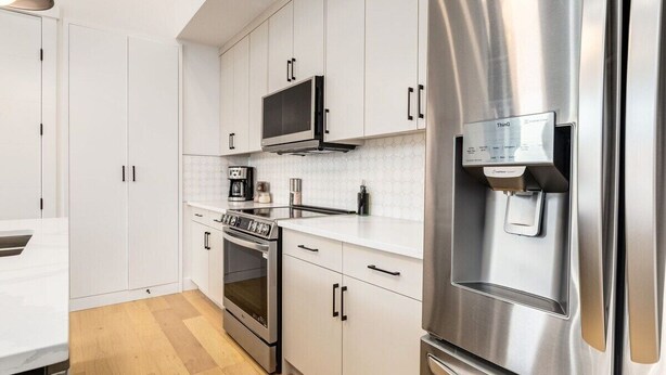 A modern kitchen with white cabinets, stainless steel appliances, and a built-in microwave. - Guest Favourite, King B, Family Friendly (Calgary)