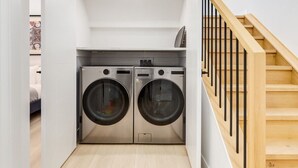 A laundry room with two front-loading washing machines, a wooden staircase, and a white interior. - Guest Favourite, King B, Family Friendly (Calgary)