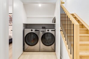 A laundry room with two front-loading washing machines, a wooden staircase, and a white interior.