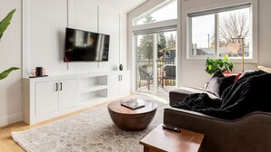 Una sala de estar moderna con un televisor de pantalla plana, un sofá, una mesa de centro y un ventanal corredero que da a un espacio exterior.