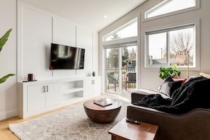 Un salon moderne doté d’un téléviseur à écran plat, d’un canapé, d’une table basse et d’une porte-fenêtre coulissante donnant sur un espace extérieur.